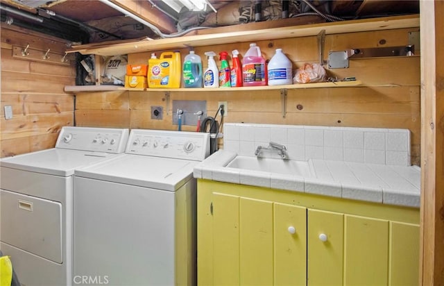 laundry area with washing machine and clothes dryer, wood walls, sink, and cabinets