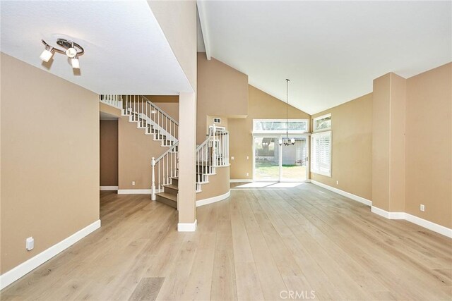 unfurnished living room with high vaulted ceiling, light hardwood / wood-style flooring, and an inviting chandelier