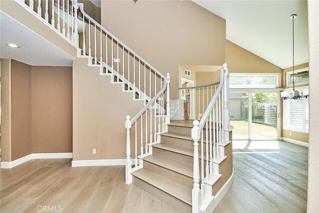 staircase with high vaulted ceiling, hardwood / wood-style floors, and a notable chandelier