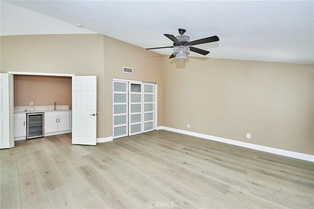 unfurnished living room with wine cooler, lofted ceiling, sink, and light hardwood / wood-style flooring