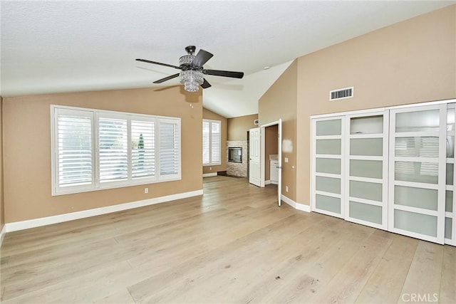 unfurnished living room featuring ceiling fan, a fireplace, light hardwood / wood-style flooring, and vaulted ceiling