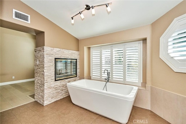 bathroom featuring a tub to relax in, vaulted ceiling, tile patterned floors, and track lighting