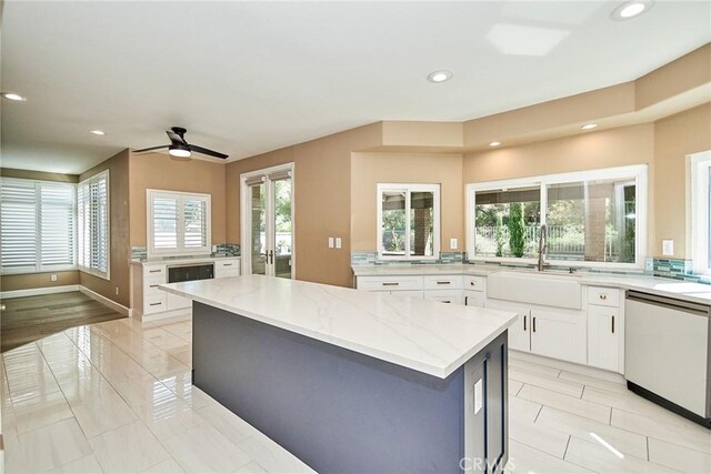 kitchen with dishwashing machine, white cabinets, a kitchen island, sink, and light stone counters