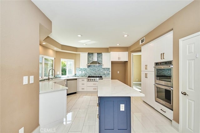 kitchen with white cabinets, appliances with stainless steel finishes, a kitchen island, wall chimney range hood, and decorative backsplash