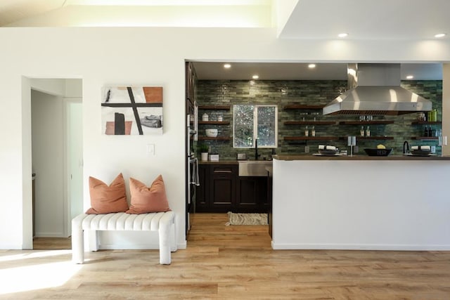 bar with brick wall, light hardwood / wood-style floors, wall chimney exhaust hood, and sink