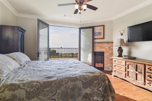 bedroom featuring a fireplace, crown molding, wood-type flooring, ceiling fan, and access to exterior