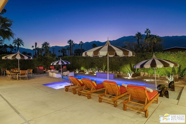 pool at dusk featuring a mountain view, a patio, and an outdoor living space