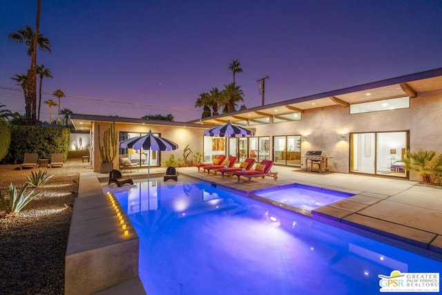 pool at dusk with grilling area, an in ground hot tub, and a patio