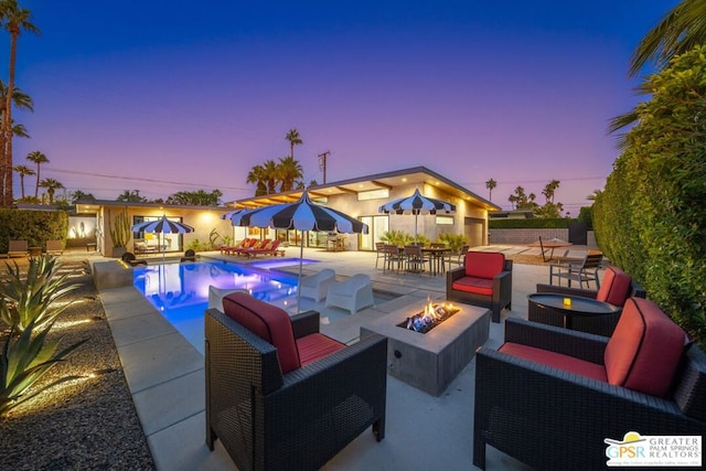 pool at dusk with a fire pit and a patio area