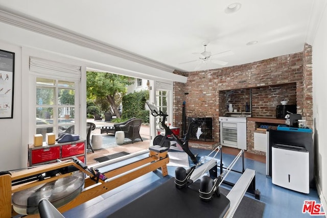 workout area featuring a wood stove, ceiling fan, crown molding, and brick wall