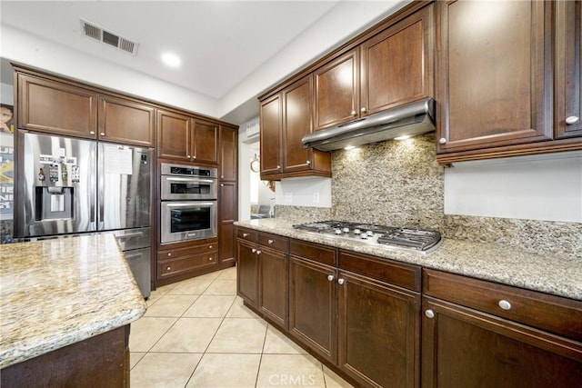 kitchen with backsplash, light stone countertops, stainless steel appliances, and light tile patterned floors