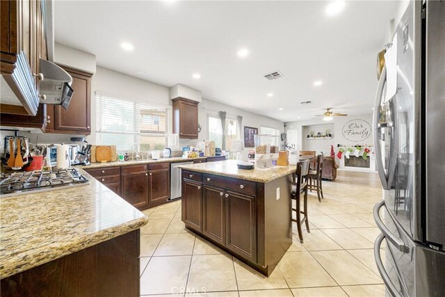 kitchen featuring ceiling fan, light tile patterned flooring, a kitchen bar, a kitchen island, and appliances with stainless steel finishes