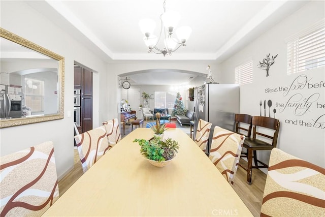 dining space with a raised ceiling, light hardwood / wood-style flooring, and a chandelier