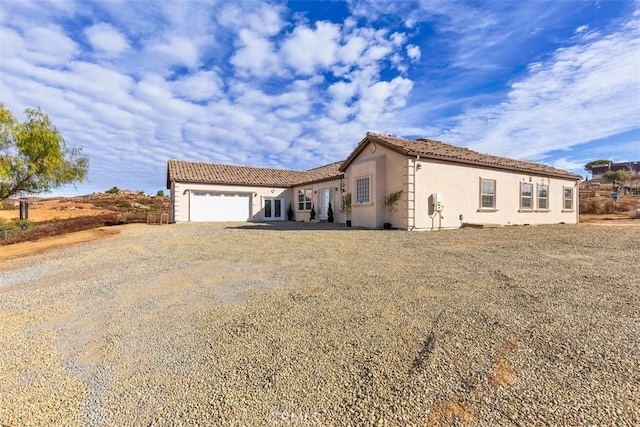 view of front of home with a garage, a tiled roof, dirt driveway, and stucco siding