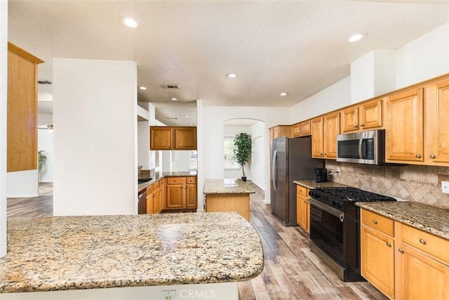 kitchen with stainless steel appliances, a kitchen island, light wood-style floors, backsplash, and light stone countertops