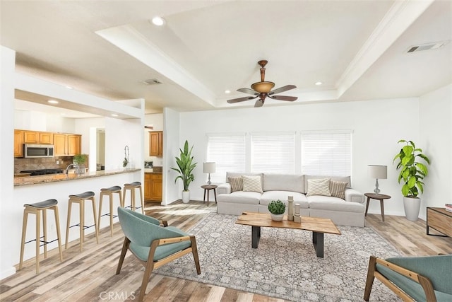 living room with ornamental molding, a tray ceiling, light wood-style flooring, and visible vents