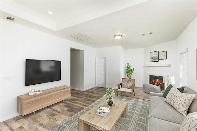 living room featuring a glass covered fireplace, visible vents, baseboards, and wood finished floors