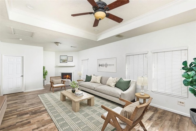 living area with a raised ceiling, visible vents, dark wood-type flooring, ornamental molding, and a lit fireplace