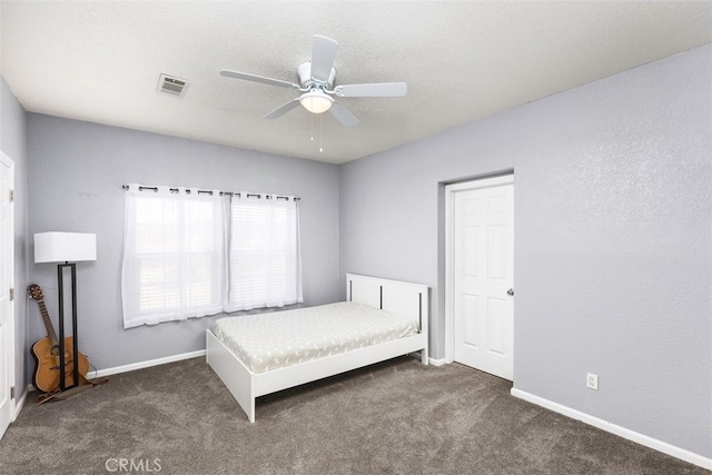 unfurnished bedroom with a textured ceiling, dark carpet, visible vents, and baseboards