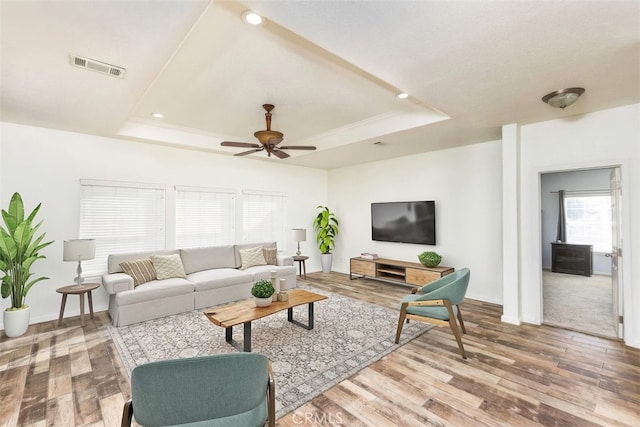 living room with a ceiling fan, visible vents, a raised ceiling, and wood finished floors