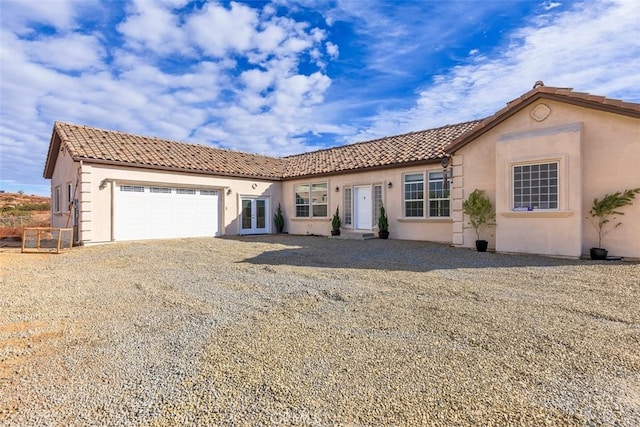 mediterranean / spanish house featuring gravel driveway, a tile roof, french doors, stucco siding, and a garage