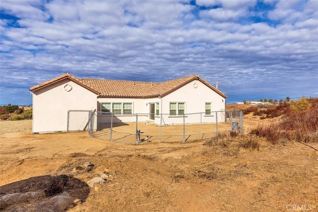 rear view of property featuring a tile roof, fence, and stucco siding