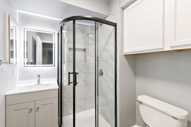 bathroom with a stall shower, a textured wall, vanity, and toilet