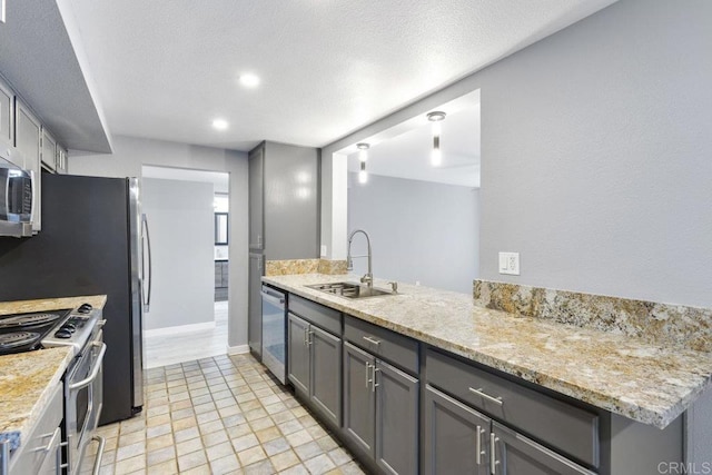 kitchen featuring a textured ceiling, light stone counters, stainless steel appliances, a sink, and gray cabinets