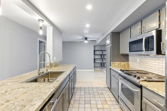 kitchen with stainless steel appliances, gray cabinets, a sink, and tasteful backsplash