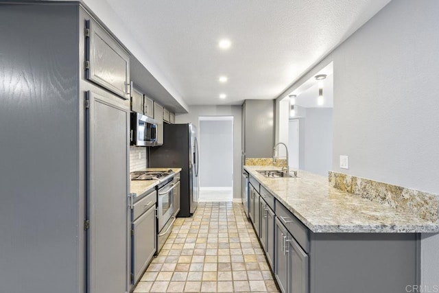 kitchen featuring backsplash, gray cabinetry, appliances with stainless steel finishes, a sink, and a peninsula