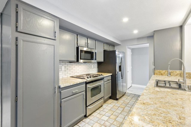 kitchen with light countertops, backsplash, gray cabinetry, appliances with stainless steel finishes, and a sink