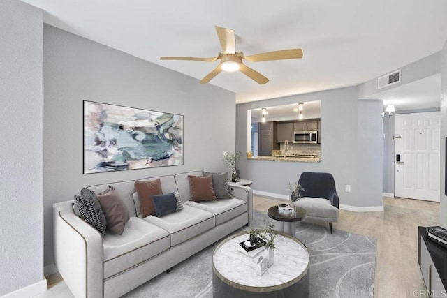 living room with baseboards, ceiling fan, visible vents, and light wood finished floors