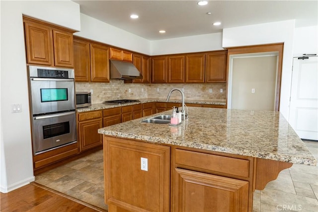 kitchen with sink, light stone counters, stainless steel appliances, and a center island with sink