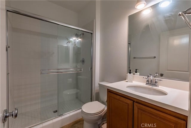 bathroom featuring toilet, vanity, and a shower with door