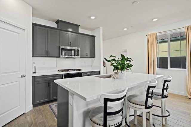 kitchen with gray cabinetry, a kitchen island with sink, a kitchen bar, wood-type flooring, and stainless steel appliances