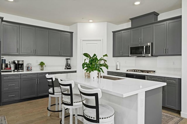 kitchen featuring stainless steel appliances, gray cabinets, dark hardwood / wood-style floors, a breakfast bar area, and an island with sink