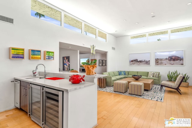 kitchen featuring light wood-type flooring, a towering ceiling, sink, and beverage cooler