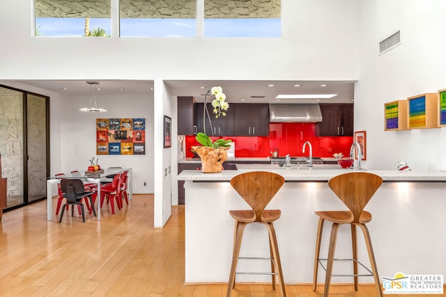 kitchen with a kitchen breakfast bar, wall chimney exhaust hood, light hardwood / wood-style floors, and a high ceiling