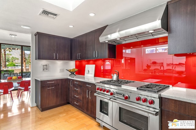 kitchen with light hardwood / wood-style floors, range with two ovens, and wall chimney range hood