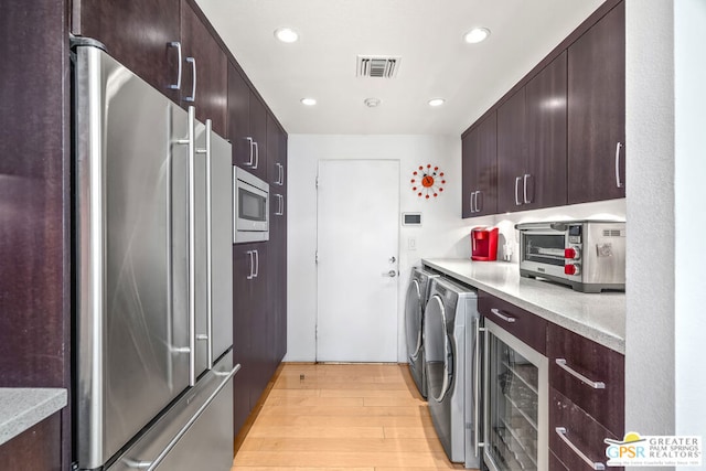 kitchen with washing machine and clothes dryer, dark brown cabinetry, wine cooler, light hardwood / wood-style flooring, and appliances with stainless steel finishes