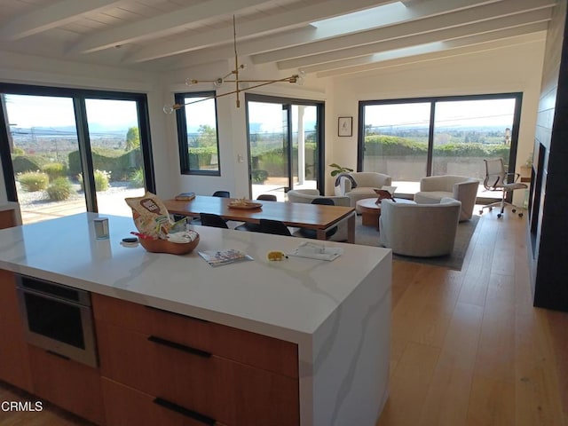 kitchen featuring a kitchen island, light hardwood / wood-style flooring, an inviting chandelier, vaulted ceiling with beams, and oven