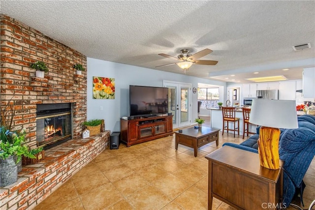 living room with a brick fireplace, a textured ceiling, and ceiling fan