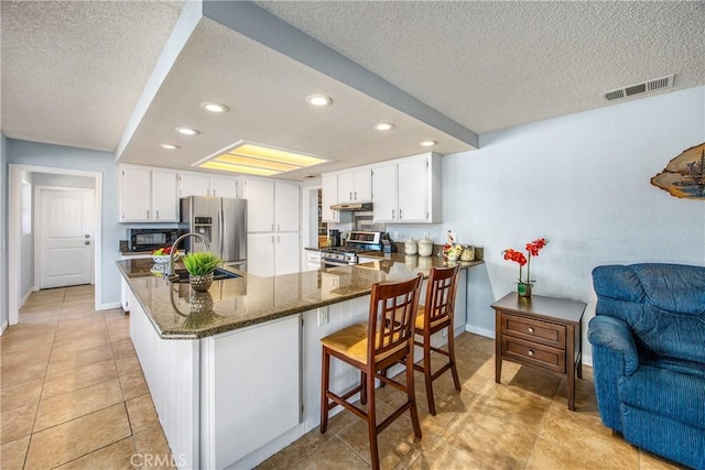 kitchen with stainless steel appliances, white cabinetry, dark stone counters, and kitchen peninsula