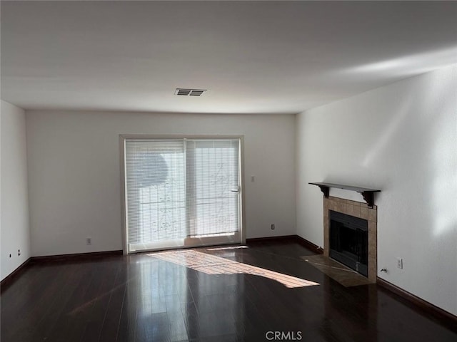 unfurnished living room with a tiled fireplace and dark wood-type flooring