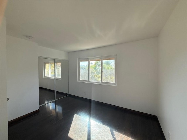 unfurnished bedroom featuring multiple windows, dark hardwood / wood-style flooring, and a closet