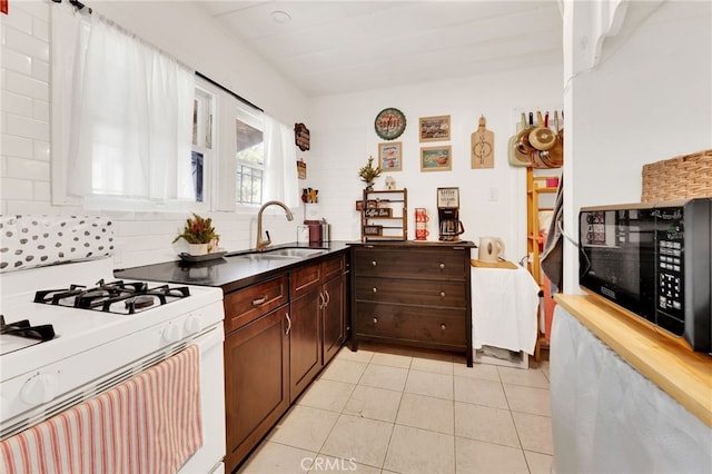 kitchen featuring sink, decorative backsplash, light tile patterned floors, white gas range oven, and dark brown cabinets