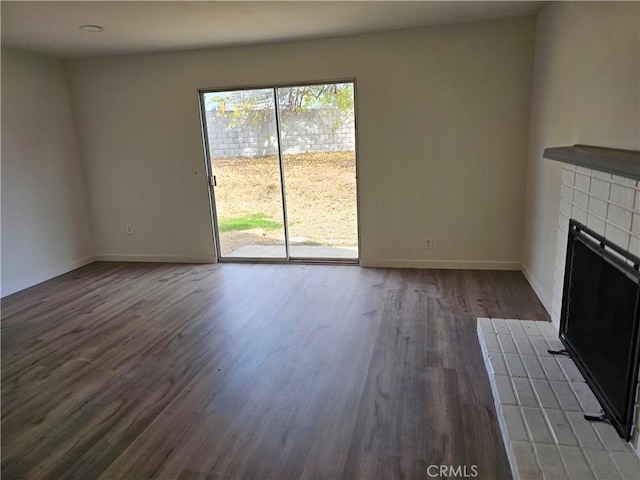 unfurnished living room featuring a tiled fireplace and dark hardwood / wood-style floors