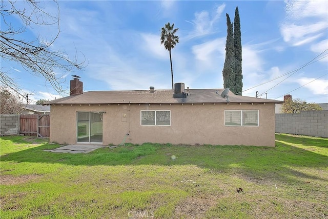 rear view of property with stucco siding, a lawn, and fence