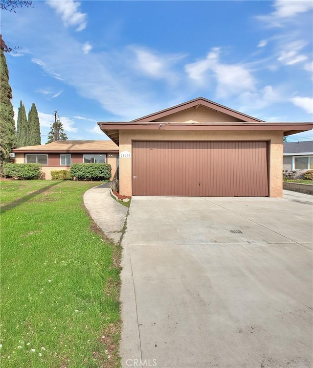 view of front facade featuring concrete driveway, an attached garage, a front lawn, and stucco siding