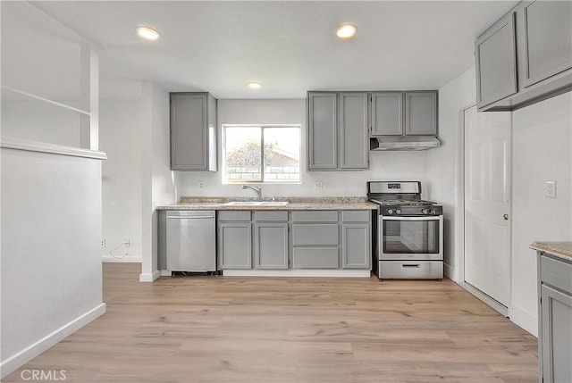 kitchen with gray cabinets, a sink, light wood-style floors, under cabinet range hood, and appliances with stainless steel finishes